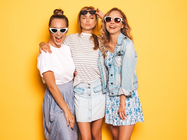 최신 유행의 여름 옷을 입고 세 젊은 아름 다운 웃는 hipster 여자. 노란 벽 근처 포즈 섹시 평온한 여자입니다. 선글라스 재미있는 긍정적 인 모델