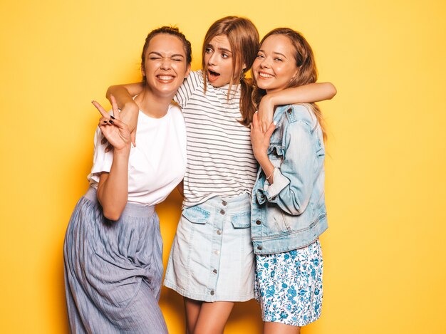 Three young beautiful smiling hipster girls in trendy summer clothes. Sexy carefree women posing near yellow wall. Positive models having fun