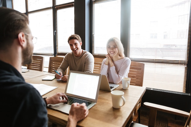 Three young cheerful colleagues work with laptops