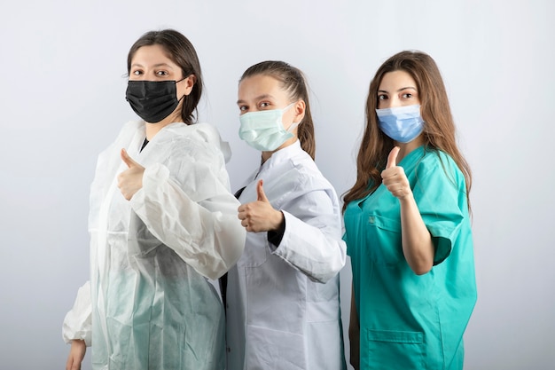 Free Photo three young female doctors standing and showing thumbs up