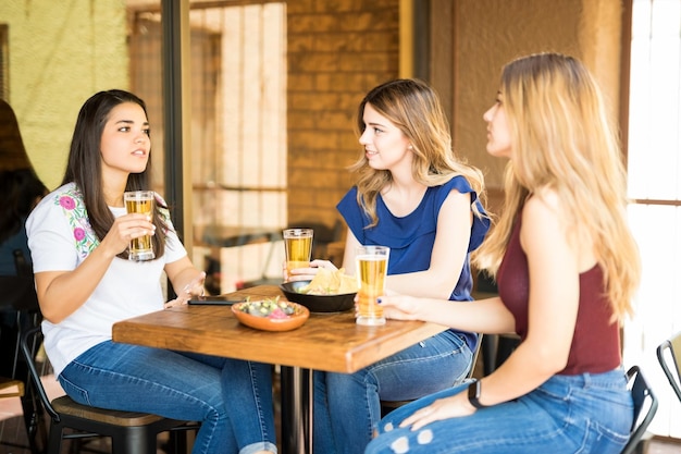 カフェでビールを飲みながらおしゃべりをしている3人の若い女性の友人