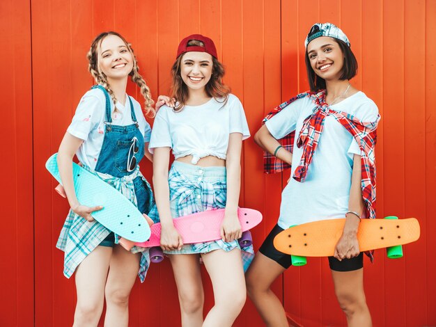 Three young smiling beautiful girls with colorful penny skateboards.