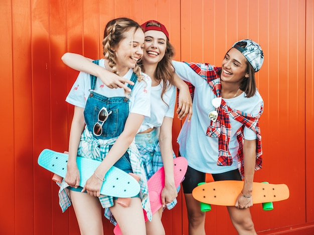 Three young smiling beautiful girls with colorful penny skateboards.