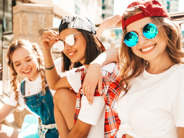 Tre giovani belle ragazze sorridenti con i pattini variopinti del penny.