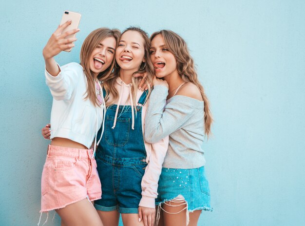 여름 옷에 세 젊은 웃는 힙 스터 여성. 소녀는 스마트 폰 selfie 셀프 초상화 사진을 찍고.