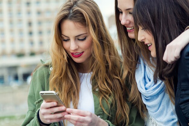 Three young women using a mobile phone in the street.