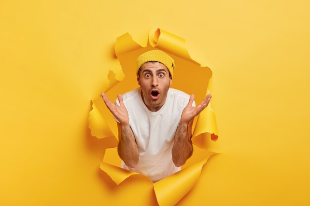 Thrilled surprised man spreads palms, stares at camera, keeps mouth opened