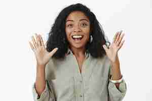 Free photo thrilled talkative happy african american woman with curly hairstyle in trendy outfit raising palms gesturing joyfully and smiling delighted