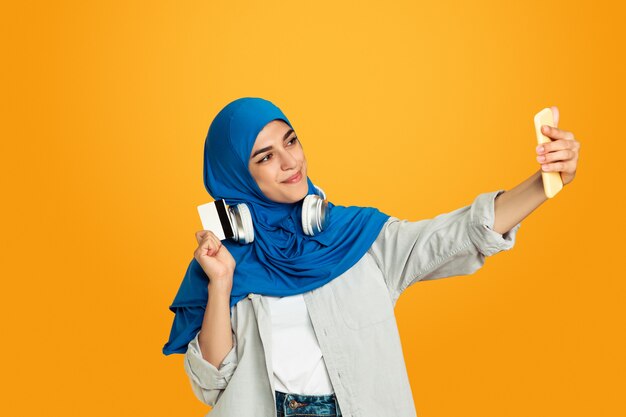 親指を立てて、音楽を聴きます。黄色の若いイスラム教徒の女性。スタイリッシュでトレンディで美しい女性モデル