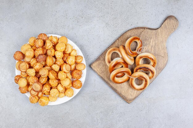 Tied ring of sushki on a wooden board next to a plate of cookies on marble surface.