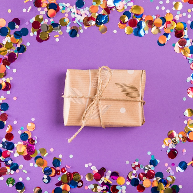 Tied string over the wrapped present surrounded with colorful confetti against purple background