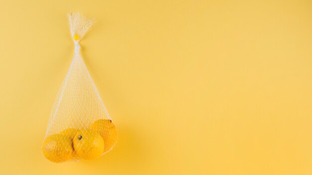 Tied up net with whole lemons on yellow backdrop