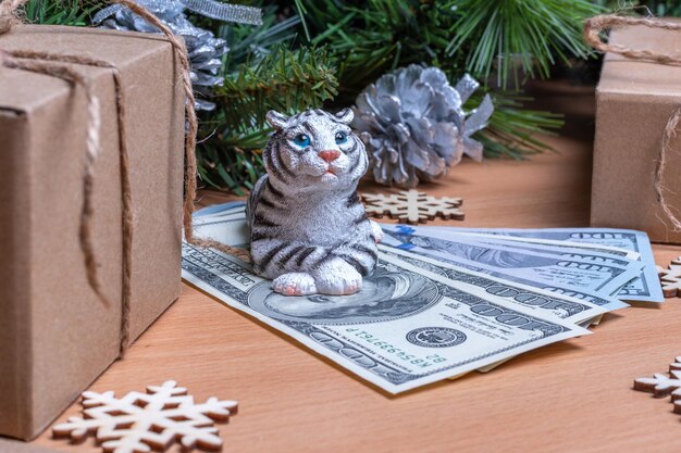 The tiger is the symbol of the chinese new year 2022. toy tiger holding cash dollars on a wooden background with gift boxes, snowflakes and fir branches with balls. success and wealth concept in 2022