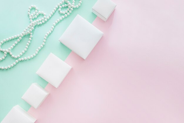 Tilt row of different white boxes with pearls necklace on pastel background