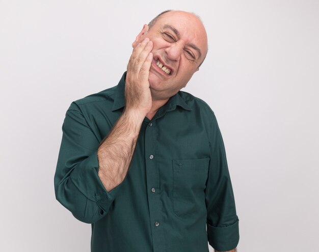 Tilting head middle-aged man wearing green t-shirt putting hand on aching cheek isolated on white wall with copy space