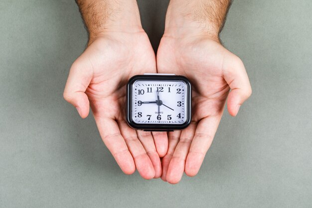 Time management and clock ticking concept with clock on gray background top view. hands holding a clock. horizontal image