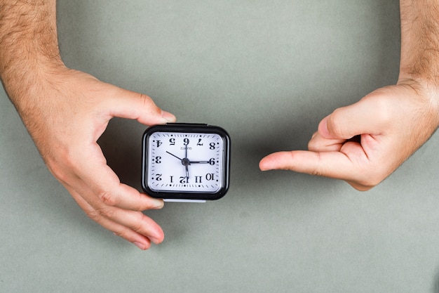 Time management and clock ticking concept with clock on gray background top view. hands holding and pointing to the clock. horizontal image