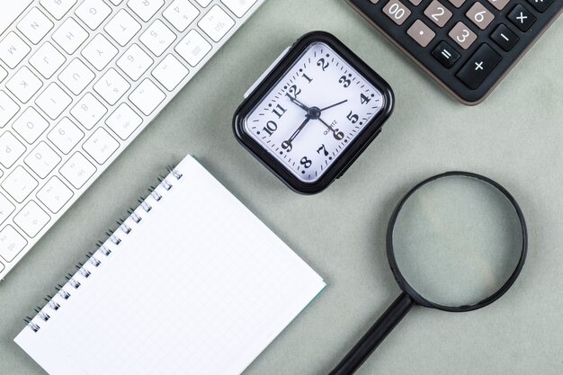 Time and money concept with keyboard, calculator, magnifier, notebook, watch on navy green background top view. horizontal image