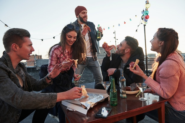 Time for singing. At least guy in red hat thinks so. Eating pizza at the rooftop party. Good friends have weekend with some delicious food and alcohol