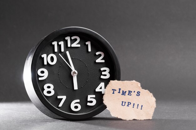 Times up blue text on torn paper near the black clock against black backdrop