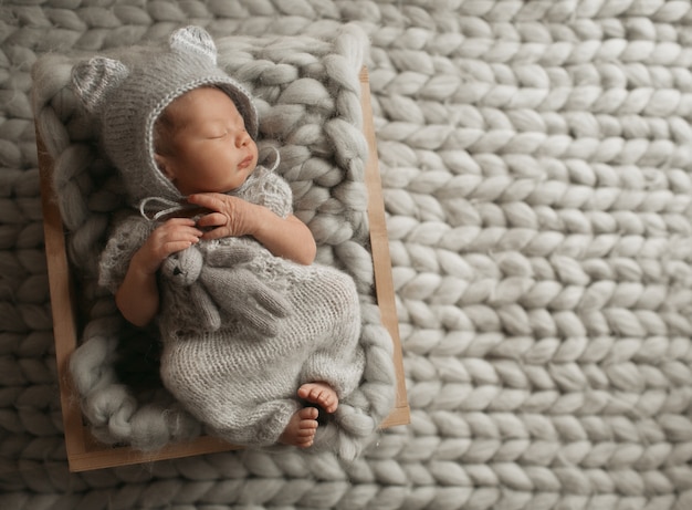 Tiny baby in grey clothes sleeps on woolen blanket