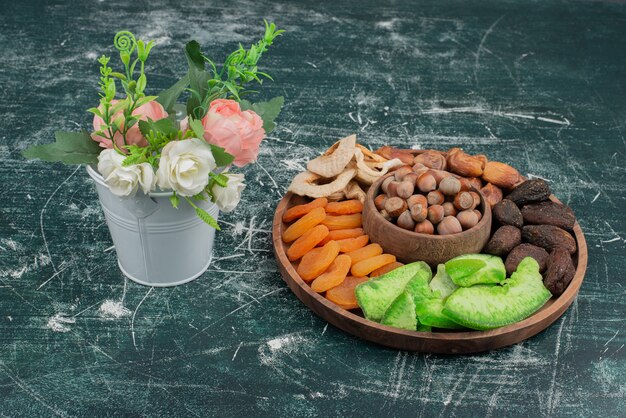 Tiny bouquet with wooden plate of dried fruits on marble surface .