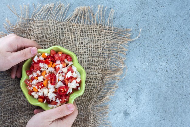 Tiny bowl of cauliflower and pepper salad held by hands on marble surface