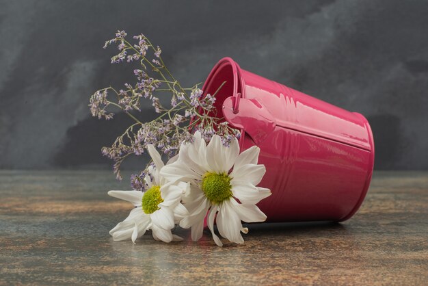 Tiny pink bucket with bouquet of flowers on marble surface. 