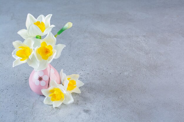 A tiny pink vase full of white flowers on gray background.