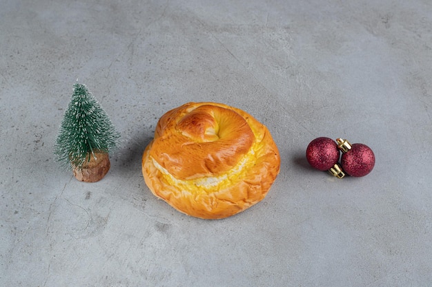 Tiny tree figurine, sweet bun and decorative balls arranged on marble table.