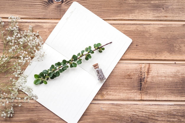 Tiny white flowers with stem and lavender flower bottle on notebook over the wooden backdrop
