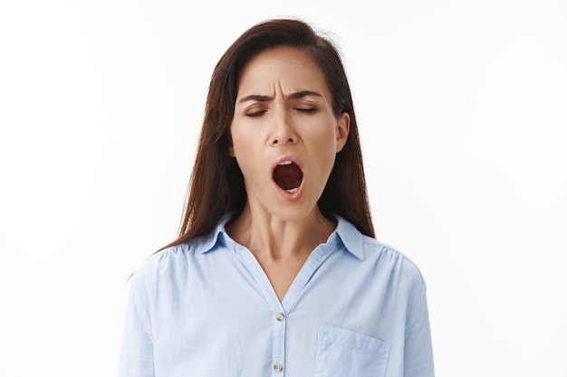 Foto gratuita donna adulta stanca donna d'affari laboriosa resta al lavoro fino a tardi, sbadigliando stanca, chiude gli occhi spalanca la bocca, si sente assonnata prosciugata, vuole dormire, svegliarsi presto la mattina, stare in piedi sul muro bianco