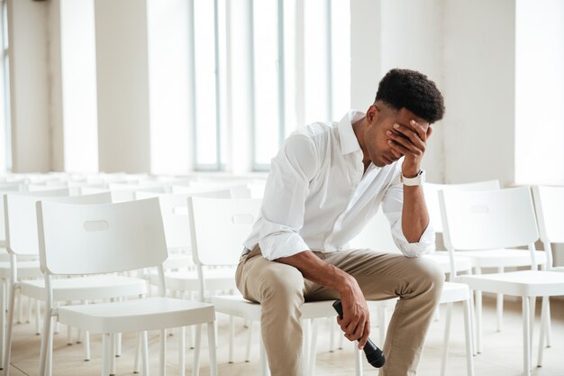 Tired african man sitting in office indoors holding microphone.