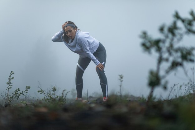 霧のかかった朝に走った後、息を切らしながら休憩している疲れた運動女性