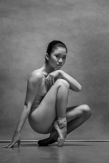 Tired ballet dancer sitting on the wooden chair on a gray