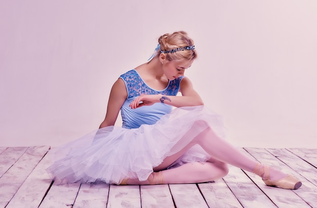 Tired ballet dancer sitting on the wooden floor