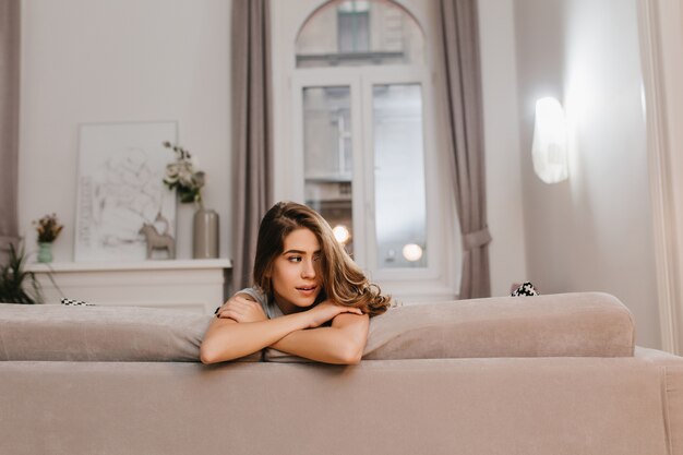 Tired brown-haired woman posing with arms crossed on sofa
