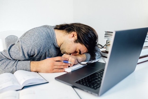 Усталый бизнесмен спит во время расчета расходов на столе в офисе. молодой кавказский служащий мужского пола дремлет в офисе на столе с планшетом и портативным компьютером ..