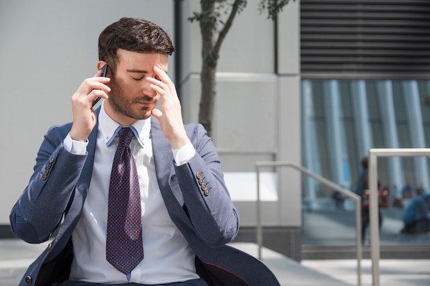 Tired businessman speaking on smartphone