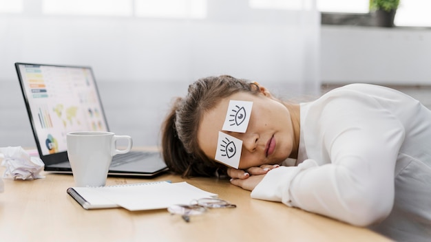 Tired businesswoman covering her eyes with drawn eyes on paper