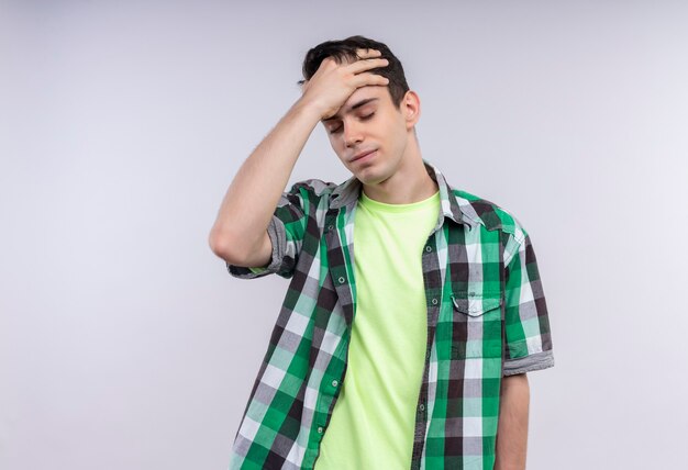Усталый кавказский молодой парень в зеленой рубашке положил руку на лоб на изолированном белом