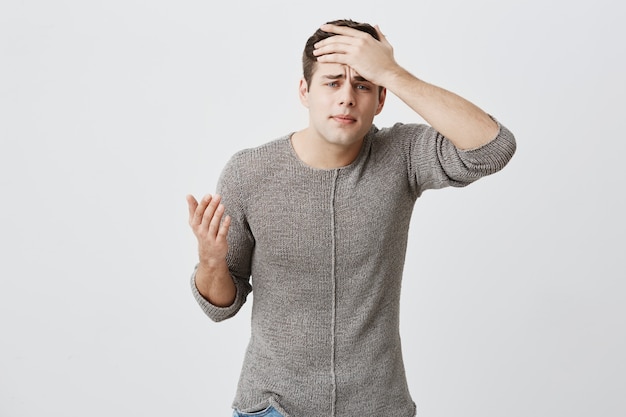 Tired dark-haired male student having headache after stress on exam. Hipster handsome man with sorrorful look holding his hand on head trying to find way out in difficult situation