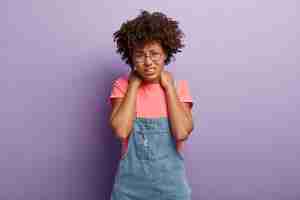 Foto gratuita la donna triste e scontenta stanca ha i capelli afro tiene entrambe le mani sul collo, sorride dal dolore, è stanca di lavorare al computer