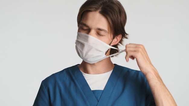 병원에서 힘든 하루를 보낸 후 졸린 의료 마스크를 복용하는 피곤한 의사 스튜디오에서 제복을 입은 젊은 인턴 과로한 표정