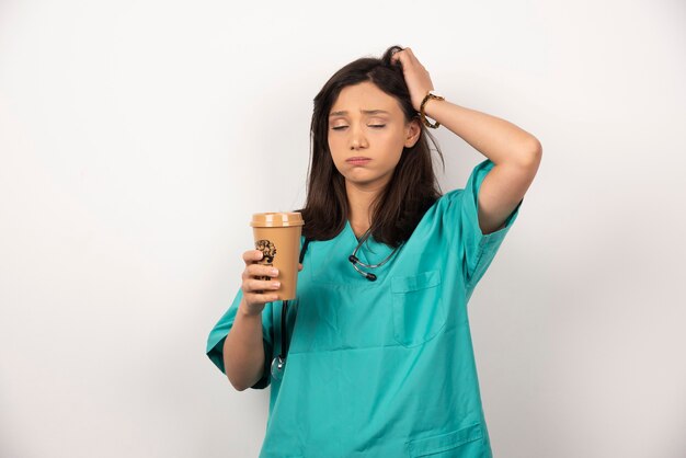 白い背景で眠っているコーヒーのカップで疲れた医者。高品質の写真