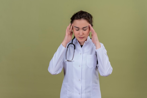 Free photo tired doctor young girl wearing medical gown wearing stethoscope puting her hands on head on green background