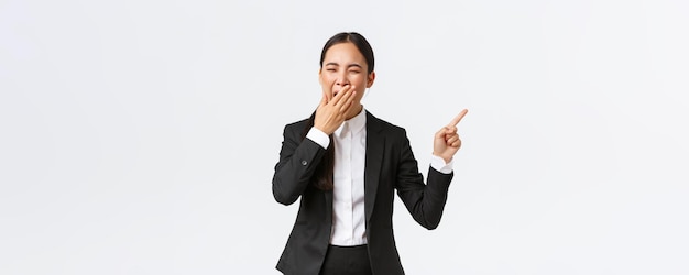 Tired female office manager entrepreneur in suit pointing finger right and yawning bored or exhauste