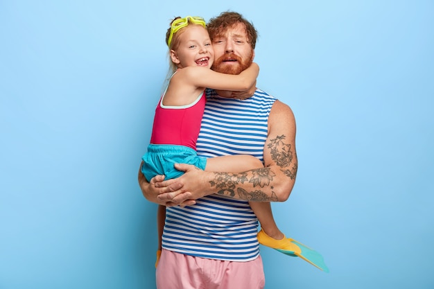 Tired ginger father and daughter posing in pool outfits