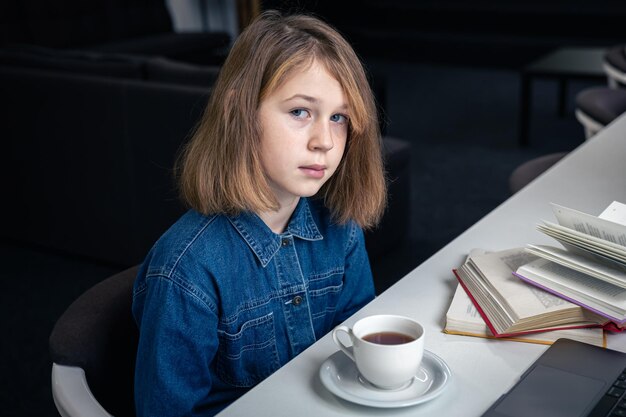 Усталая девушка перед ноутбуком с чашкой чая и книгами