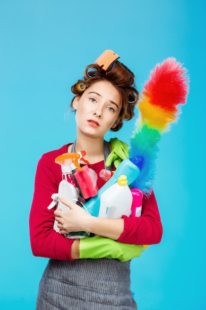 Tired housewife in pink outfit holds duster and cleaning tools